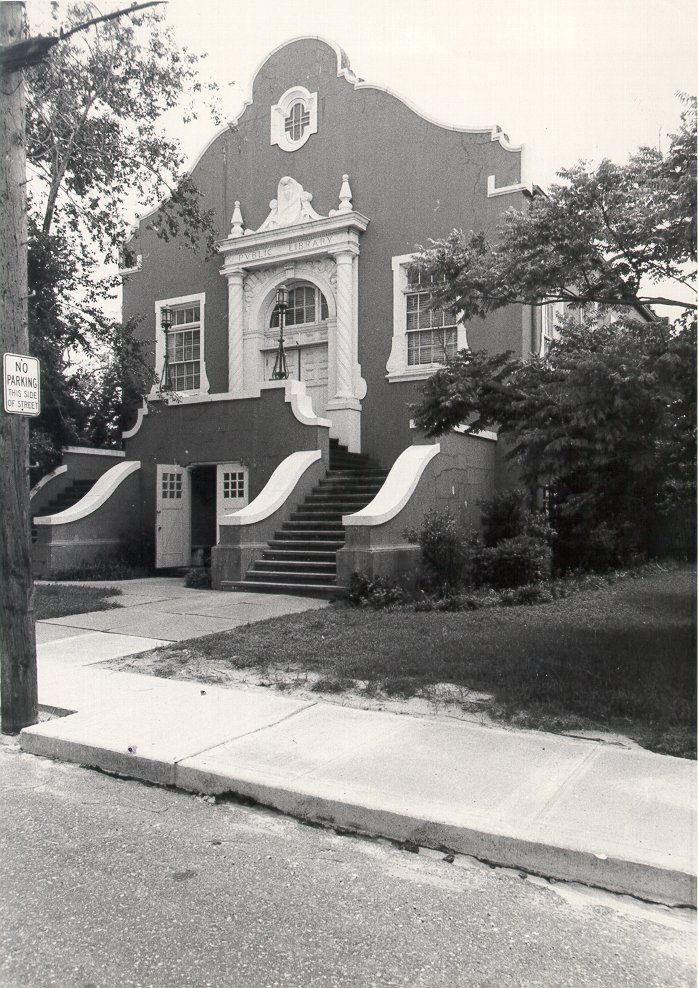 A black‑and‑white photograph of a two‑story building with ornate architectural details, featuring a central arched doorway, curved exterior staircases on both sides, and tall windows framed with decorative trim.