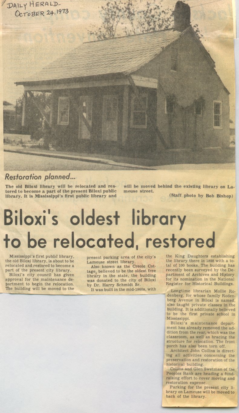 A newspaper clipping titled “Biloxi’s oldest library to be relocated, restored” from the Daily Herald dated October 24, 1973. The article explains plans to move and restore Mississippi’s first public library, known as the old Biloxi Library, to become part of the present Biloxi Public Library. The photo shows a small wooden cottage with a triangular roof, front porch, and multiple windows, described as the historic library building.