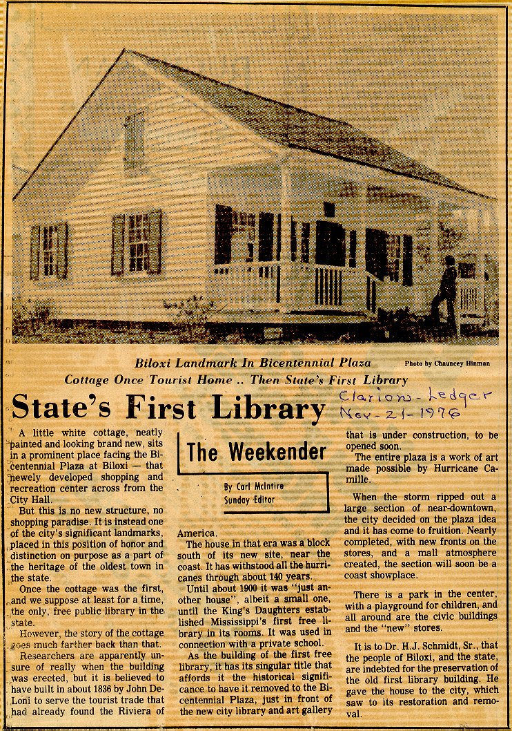 A newspaper clipping titled “State’s First Library” with the subtitle “Biloxi Landmark in Bicentennial Plaza.” The article describes a historic white cottage, once a tourist home and later Mississippi’s first public library, now located in Biloxi’s Bicentennial Plaza. The photo shows a small white wooden cottage with a triangular roof, front porch, and four columns, with a person standing near the entrance.