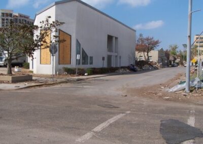 The exterior corner of the library is shown with boarded windows and large piles of debris pushed against the building. Surrounding streets contain scattered trash and storm damage.