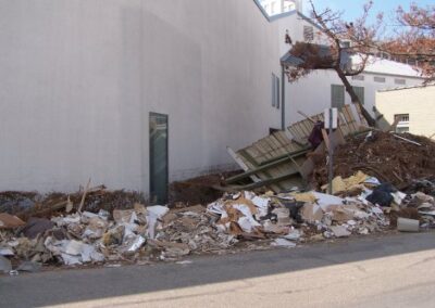 A large pile of storm debris—including wood, drywall, and library furnishings—rests along the exterior wall of the library. The ground is covered in scattered rubble and flood‑damaged materials.