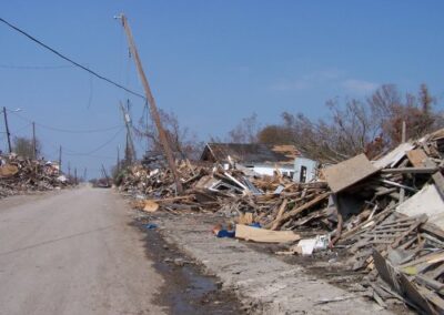 A neighborhood street is filled with storm wreckage, including splintered lumber, roofing material, and household debris piled along both sides. Leaning utility poles and stripped trees show the extent of the destruction.