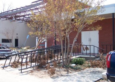 A wide overhead view of a devastated library floor filled with toppled media racks, scattered books, mud, and debris illuminated by sunlight from broken windows. Structural supports and shelving show extensive storm damage.