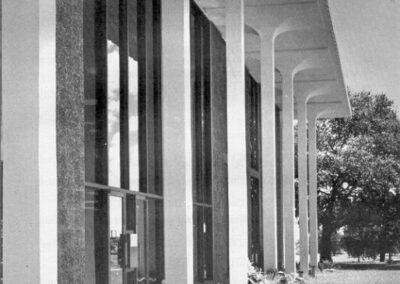 A black‑and‑white image of the library’s exterior showing tall columns, floor‑to‑ceiling windows, landscaped planters, and a reflecting pool, overlaid with text announcing the formal dedication of the Gulfport‑Harrison County Library on November 27, 1966.