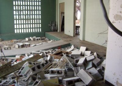 A large pile of cinderblocks, broken boards, and construction debris fills a damaged room inside the Gulfport Library. Open doorways and a green painted wall are visible behind the rubble.